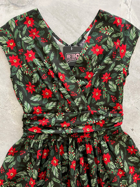 Mid length cotton dress with surplice neckline, cap sleeves, wide cummerbund style waistband, and full skirt. In a red and green holly, poinsettia, and mistletoe pattern on a black background. Shown flat in close up of bodice
