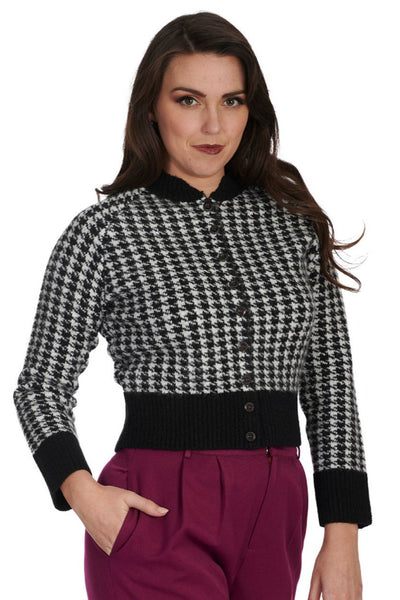 retro style long sleeve waist length button-up cardigan in a knitted black &amp; white houndstooth pattern with solid black ribbed knit waistband, cuffs, and stand-up collar. shown worn by a model