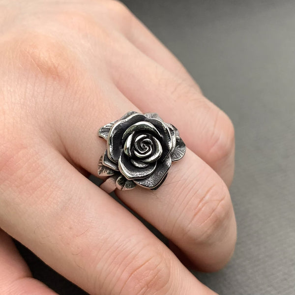 silver stainless steel ring in the shape of a blossoming camellia flower and its leaves. Shown worn
