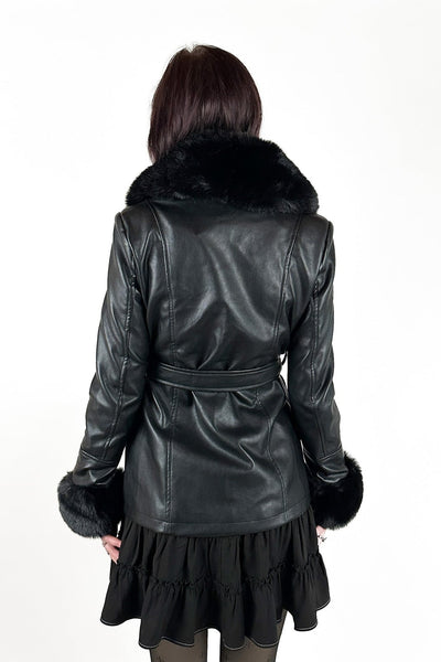 model wearing a black faux-leather wrap coat with a large black faux fur shawl collar, matching fur-trimmed cuffs, and a self-tie belt. Shown from back closed