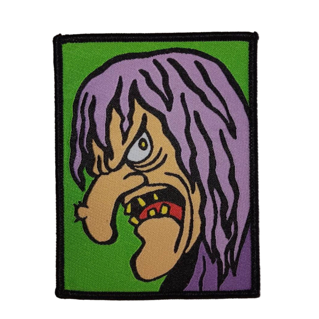 Rectangular woven patch of a witch with purple hair, yellow teeth, and a large warty nose on a green background