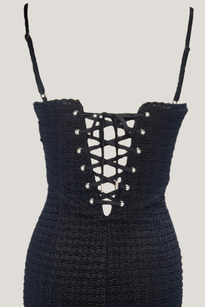 Black waffle knit bodycon mini dress with adjustable spaghetti straps, vertical seaming, and black lace trim at bodice and  bottom hem. Shown from back in close up of back bodice to show corset style lace up back with silver metal grommets and black ribbon 