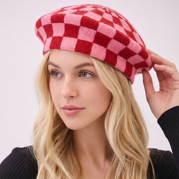 Woman wearing a red and pink checker patterned knit beret against a plain background