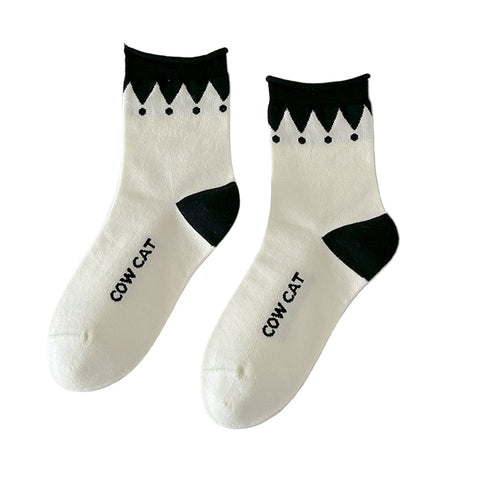 Pair of white socks with black pointed jester style accents and 'COW CAT' text on bottom of sock