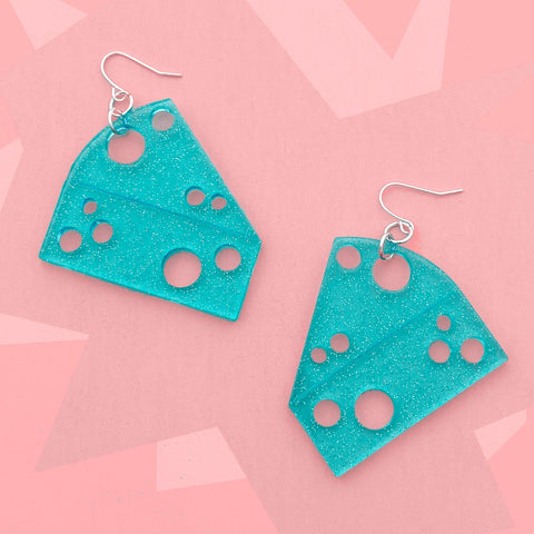 Dangle earrings made of transparent sparkly blue laser-cut acrylic in the shape of two pieces of cheese, full of holes. On a bright pink background 