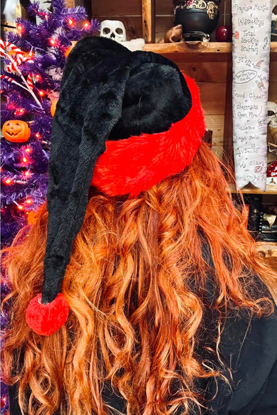 Santa style stocking cap in faux fur with black body and red trim and Pom Pom. Shown worn by a model from the back