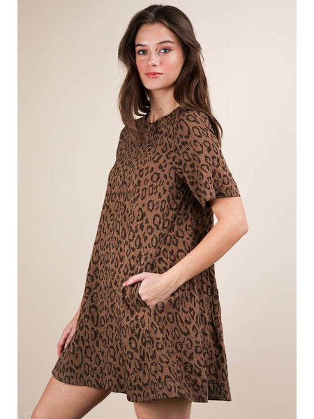 Model wearing a brown leopard print short sleeved a-line mini dress with a rounded collar and side seam pockets. Shown from the side with one hand in pocket