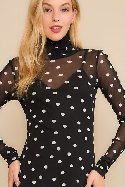 Model wearing a black and white polka dot mesh midi length dress with long sleeves. It has a matching black v-neck spaghetti strap slip underneath. Shown from the front in close up