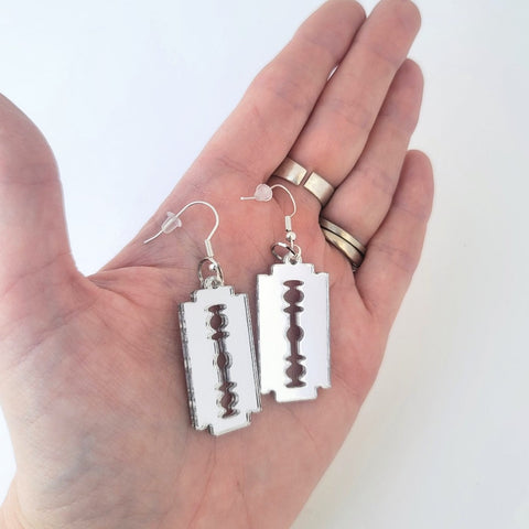 Small silver mirrored laser cut acrylic razor blade shaped dangle earrings. Shown held in a hand to illustrate size