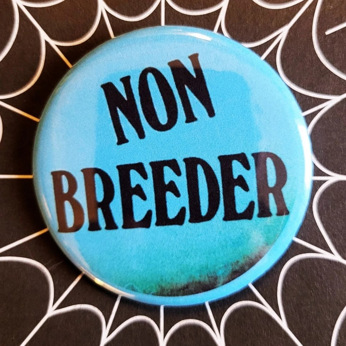 1.25” round button with “NON BREEDER” written in black on bright blue background 