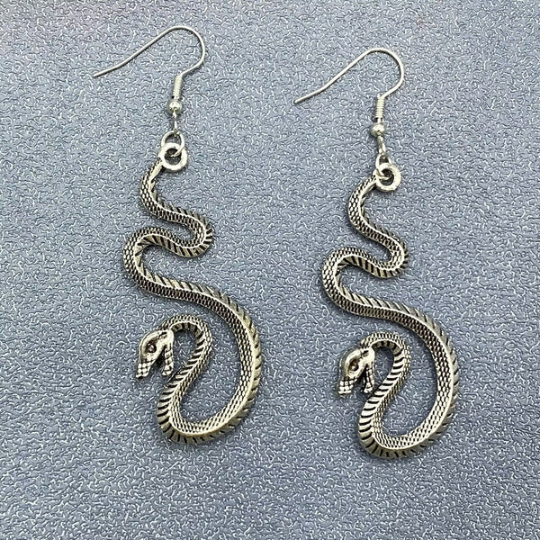 Pair of burnished silver metal hissing detailed snake dangle earrings. Shown flat