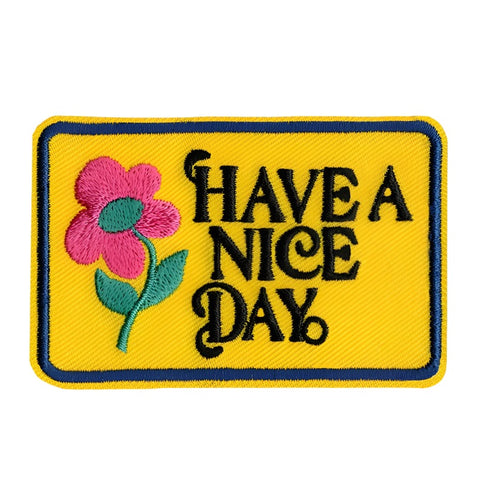 rectangular yellow embroidered patch with navy blue border and green & pink daisy alongside "HAVE A NICE DAY" written in black script