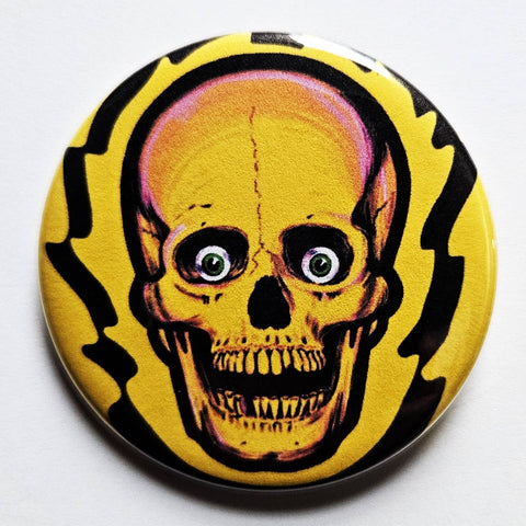 1.25" round pinback button with retro yellow and pink skull with green eyeballs on jagged flame-like black and yellow background