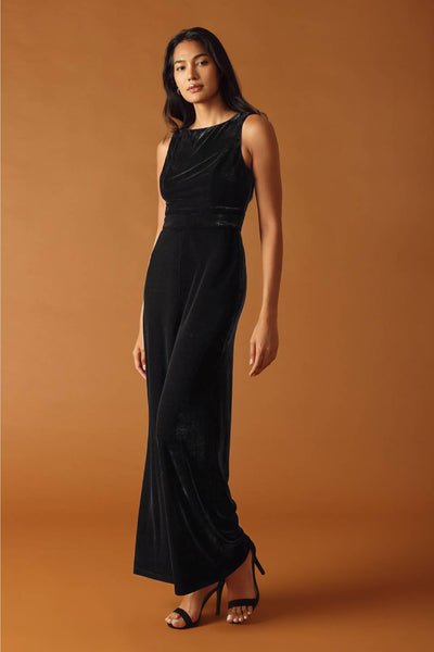 model wearing black velvet jumpsuit with boatneck and seamed sleeveless bodice, banded waistband, and wide legs. Shown from front at 3/4 angle
