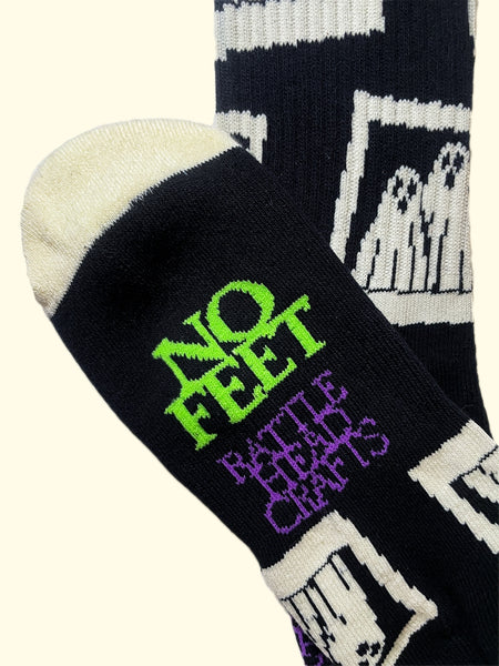 black cotton unisex crew socks with an all-over print of instant film camera pictures of a pair of ghosts wearing sheets. Bottom of foot shown with purple and green writing "NO FEET" "RATTLEHEAD CRAFTS"