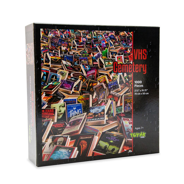 1000-piece jigsaw puzzle box titled 'VHS Cemetery'. The packaging features a collage of various retro VHS horror movie tapes in a cluttered pile, set against a black background with red and white text.