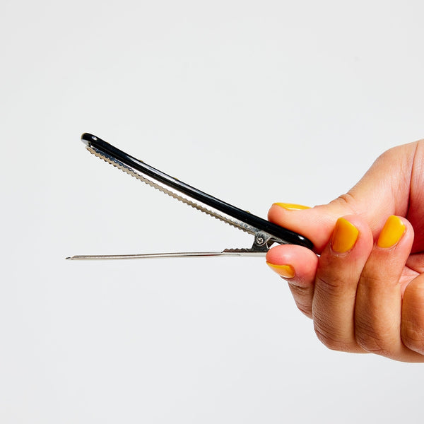 black acetate curved hair clip with flat top decorated with row of 6 clear rhinestones and alligator clip backing. Shown held from side to display hardware while open