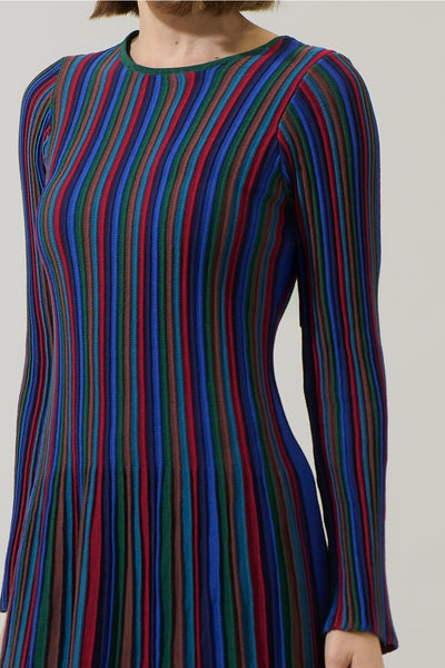 model wearing a fully lined sweater dress in a vertically striped ribbed pattern in jewel tones of blues, reds, greens, and amber. Dress is a mini length with flared skirt and slightly flared cuff long sleeves. Shown from front in close up of pattern