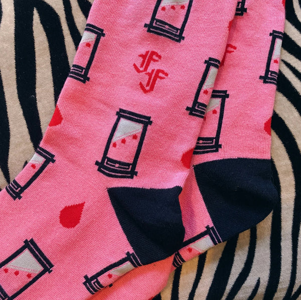 Pink socks with black guillotines and red drops of blood and black toes, cuffs, and heels on a zebra-patterned surface. Shown in close up