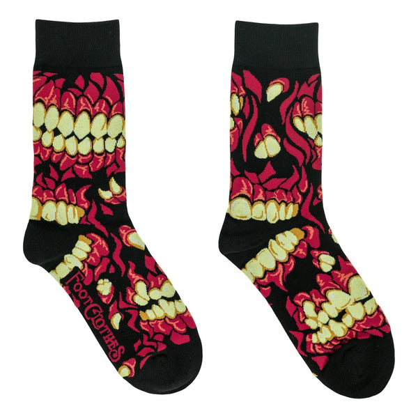 A pair of unisex cotton blend crew socks with a black background and an allover pattern of a skull's teeth and mouth in red and pale yellow. Shown flat