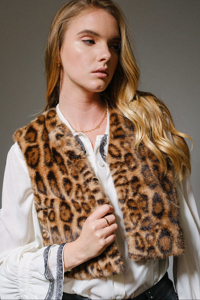 Woman wearing a leopard print vest over a white shirt on a gray background. Shown from front in close up