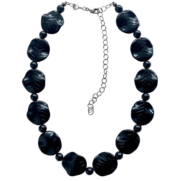 16" necklace made of black disc beads with carved leaf detail alternated with small round black lucite beads. Shown flat on white background
