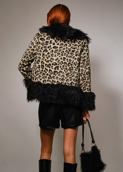 Woman wearing a leopard print coat with a black shaggy fur collar, cuffs, and bottom hem against a gray background. Shown from back