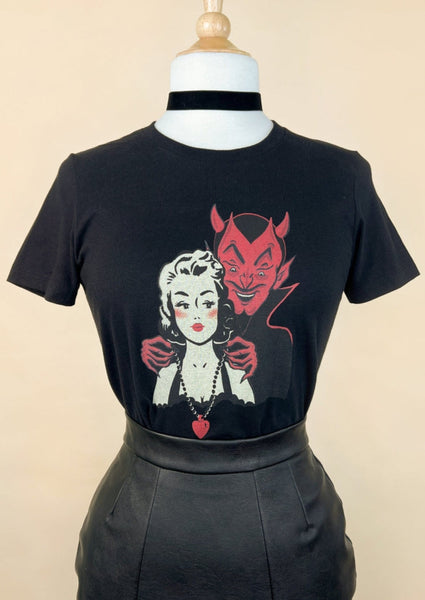 a fitted black cotton t shirt with a retro illustration of a devil putting a heart shaped necklace around the neck of a pinup style woman with blonde hair. Shown on a dress form tucked in