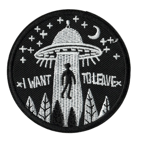Embroidered patch with a silhouette of a person facing a UFO and text 'I want to leave' on a black background.