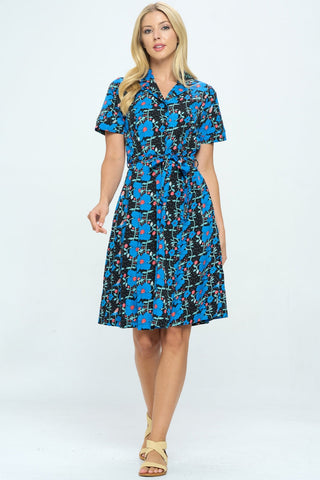 Model wearing black background blue and pink floral vertical vine print shirtwaist dress with notched v-collar, short sleeves, self sash, pockets, and a just above the knee flared skirt. Shown from front