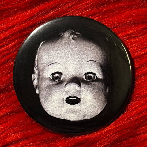 Black and white photo of a doll's head on a 2.25" pinback button on a red textured background