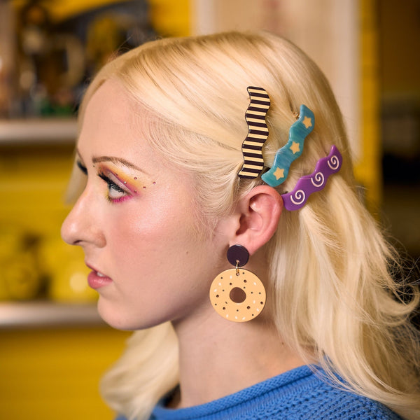 three acetate barrettes in a wavy rectangular shape with unique patterns (lavender spirals on purple background, black and cream stripes, pale yellow stars on marbled blue background) shown in model's hair from side