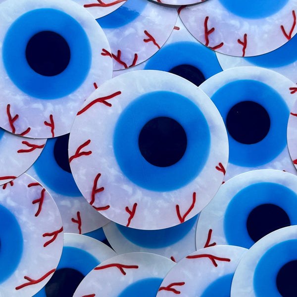 die-cut glossy finish vinyl sticker of cartoony bloodshot eyeball with marbled white and light blue iris with black pupil. Shown in pile of eyeball stickers 