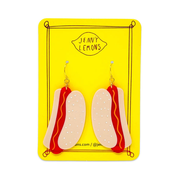 cellulose acetate dangle earrings in the shape of a pair of hot dogs in buns with yellow wavy mustard detail. Shown on backing card