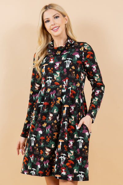 model wearing a knit long sleeved dress in a black background multicolored woodsy mushroom print. it has a cowl style neck, pockets, and knee length skirt. Shown from the front in close up