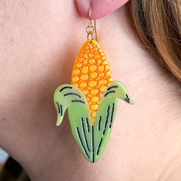 cellulose acetate dangle earrings in the shape of yellow ears of corn with half-shucked green husks and black painted detail. Shown on model