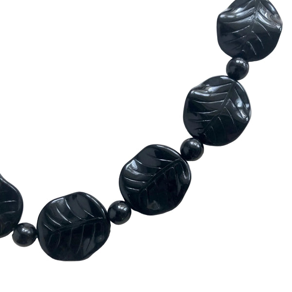 16" necklace made of black disc beads with carved leaf detail alternated with small round black lucite beads. Shown flat in close up of bead detail on white background