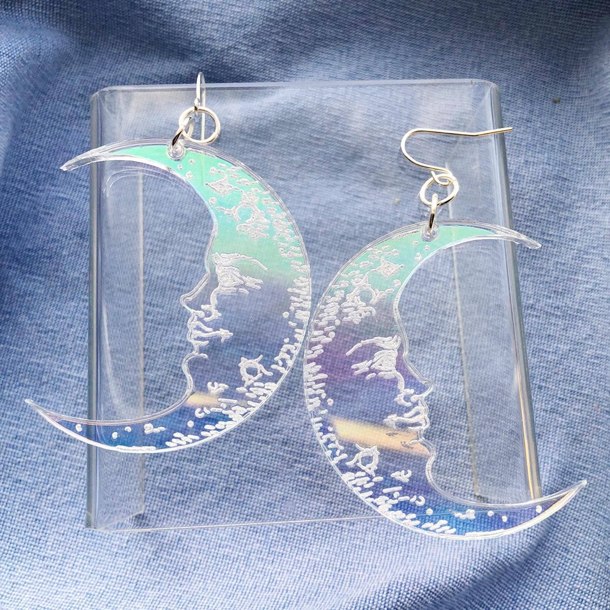 a pair of clear acrylic iridescent flash finish dangle earrings in the shape of two crescent moons with etched face detail