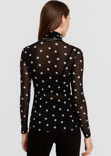 model wearing a black mesh turtleneck top with an allover print of white polka dots. Shown from back