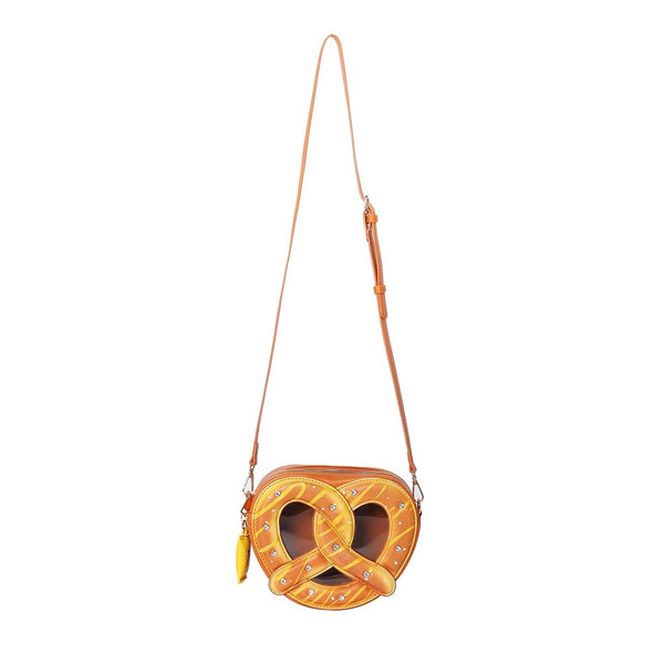 A brown faux leather crossbody purse in the shape of a large pretzel with mustard packet-shaped zipper pull, large rhinestones as grains of salt, and brown vinyl window. Shown from front with crossbody strap attached
