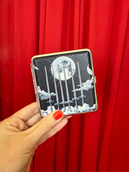Cigarette case with six of swords tarot card celestial black and white design featuring a moon and six swords against clouds. Shown held closed in front of a red velvet background