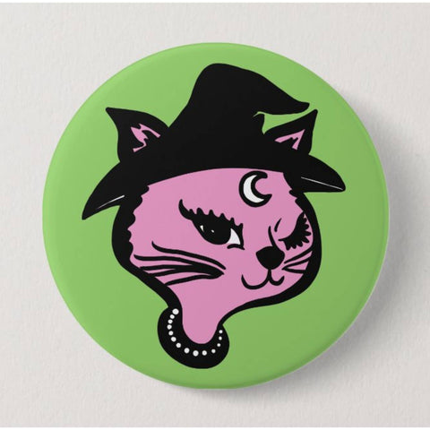 Circular button with pink cat wearing a black witch hat on a green background