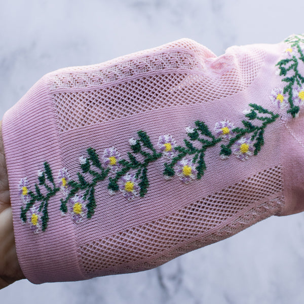 Light pink cotton socks with a knit-in pattern of purple, white, and green flowers and panels of patterned mesh. Shown held stretched to show mesh