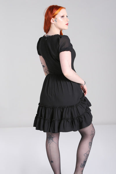 black mini dress featuring princess seamed fitted bodice with a lace edged angled v-neckline and velvet bow detail at the bust, sheer puffed short sleeves with elasticized cuffs, and a gathered full above the knee length skirt finished with a double row of flounces. shown back view on model.