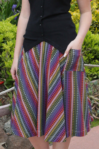 model wearing stretch cotton midi a-line skirt with 3" waistband and patch pockets in black background pattern of micro florals and leaves in bright colored stripes