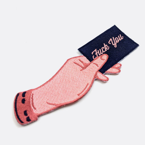 embroidered patch of a pink hand holding a rectangular card in navy blue with message "Fuck You" written in pink cursive