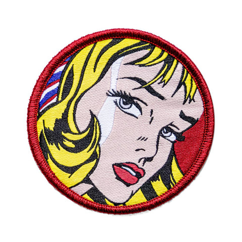 Circular patch with woven image of detail from Roy Lichtenstein painting of blonde woman on red background with red embroidered border