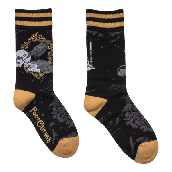 black unisex crew socks with a grey damask pattern, mustard and black striped cuffs, and mustard heels/toes. Ankle design is a raven perched on a stack of books alongside a skull, candlestick, and cup of tea. Shown flat