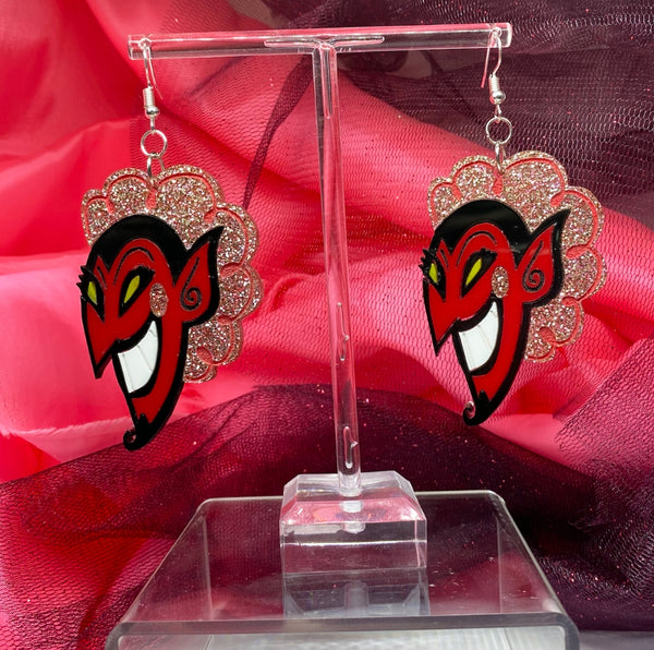 laser cut acrylic dangle earrings with pair of charms in the shape of the face of HIM from Powerpuff Girls with glittery pink hair and cheeks. Shown on red and black tulle background
