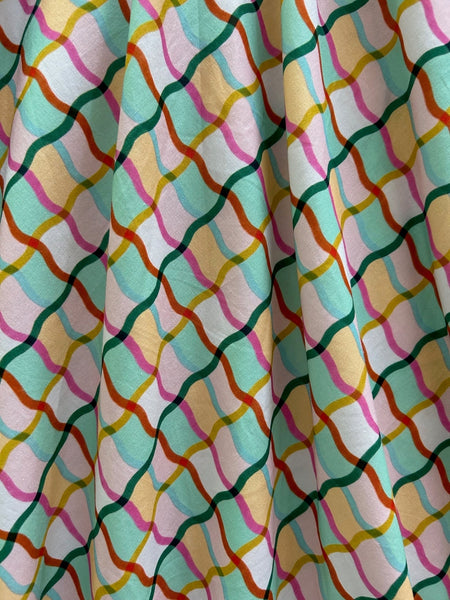 dress with surplice style neckline, cap sleeves, wide cummerbund style waistband, and full below the knee skirt with pockets. All-over print of wavy windowpane pattern in overlapping shades of light pink, teal, red, mustard, and minty green. Shown laid flat in close up of skirt to show print